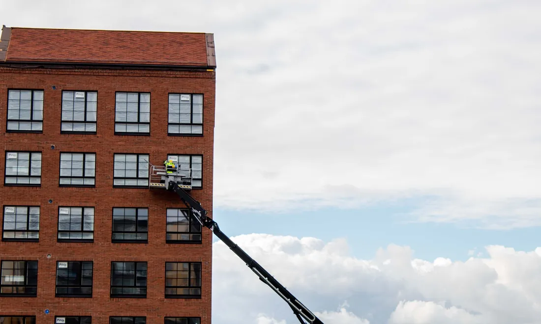 Arbeiter auf einer Hubarbeitsbühne vor der Fassade eines Backsteinhauses